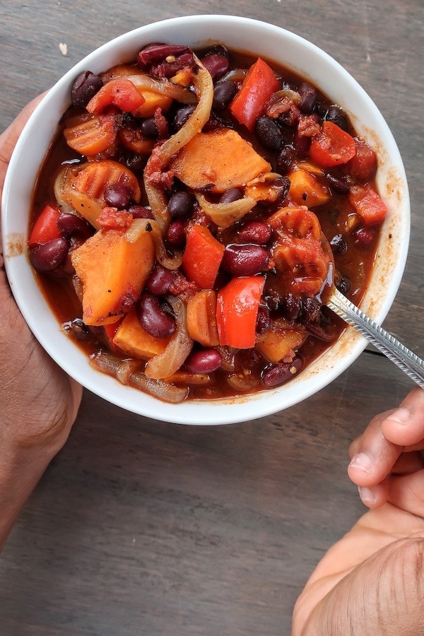 Sweet potato chili in white bowl with hand holding spoon.