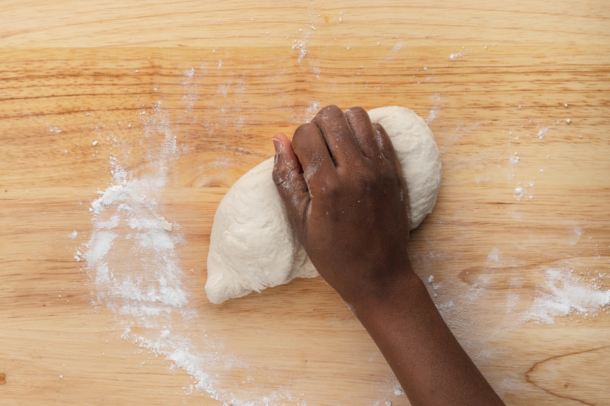 hand kneading pastry dough on wooden cutting board.