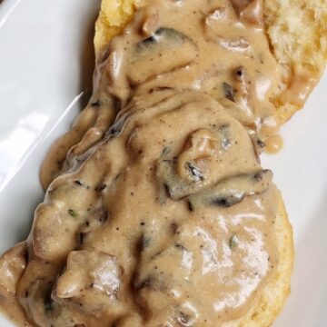 close up of vegan biscuit covered with mushroom gravy on a white plate