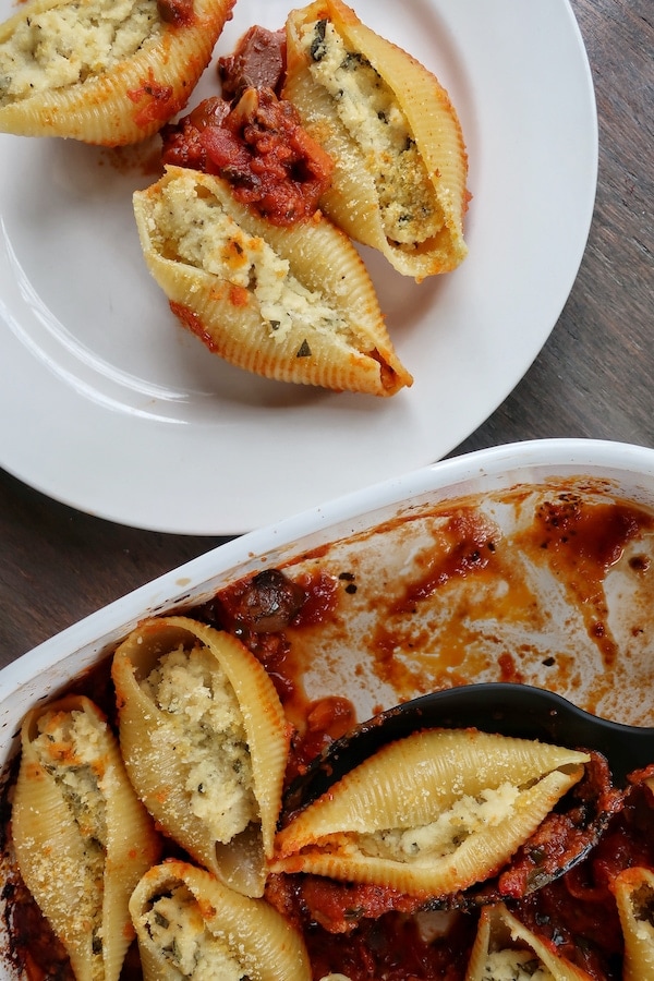 Three vegan filled pasta shells on white plate next to casserole dish