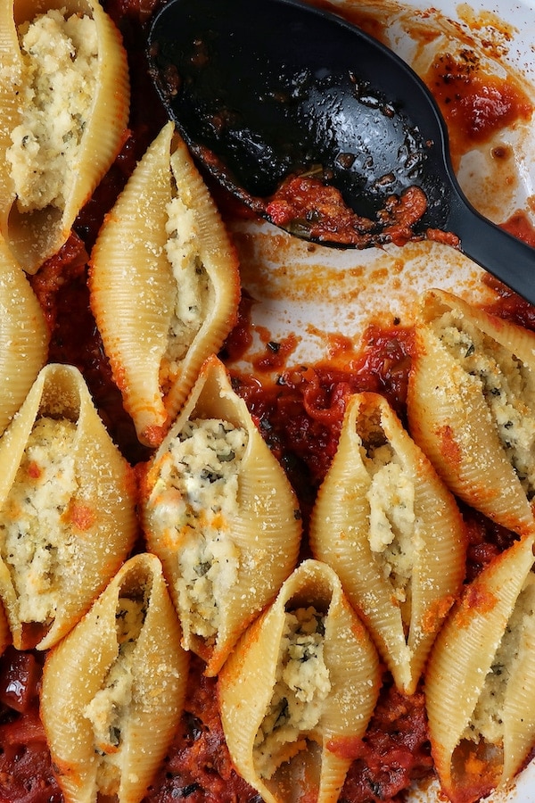 Vegan stuffed shells with almond ricotta in white casserole dish with big spoon