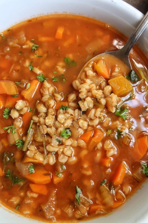 Close up of vegetable barley soup in a white bowl with a spoon