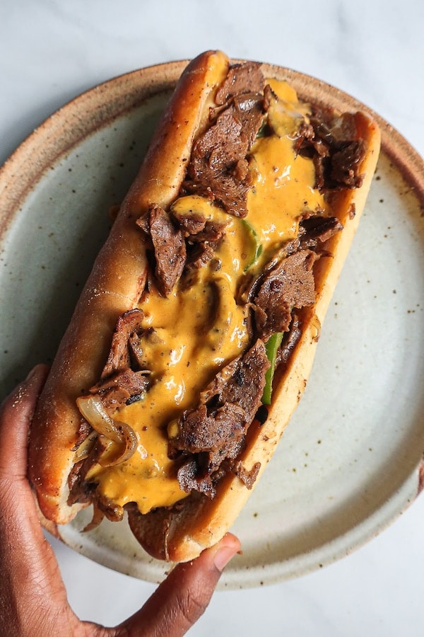 Vegan philly cheesesteak sandwich on a plate held by one hand