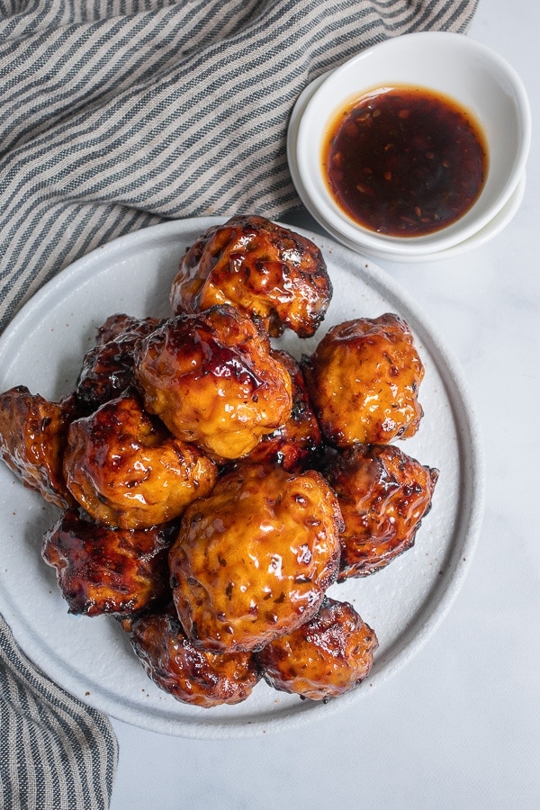 Air fryer cauliflower on a white plate next to bowl of teriyaki sauce and striped cloth