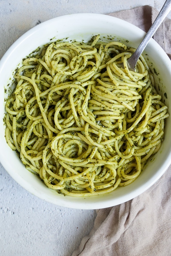 Pasta with kale pesto in a bowl with a fork on a kitchen towel