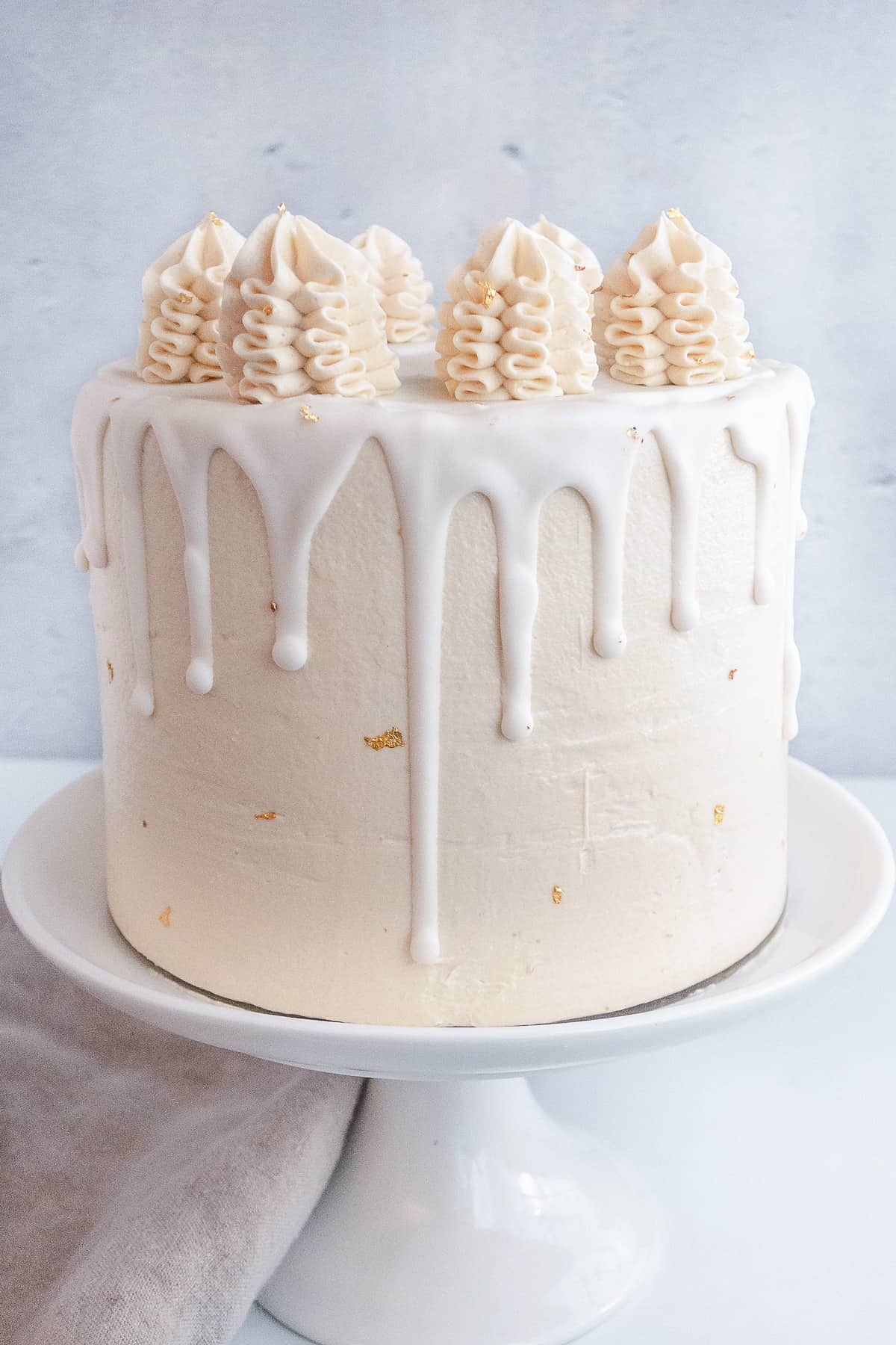 Vanilla cake with drips and piped frosting on a white cake stand