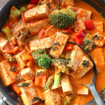 thai tofu curry and vegetables in a pan with a large spoon