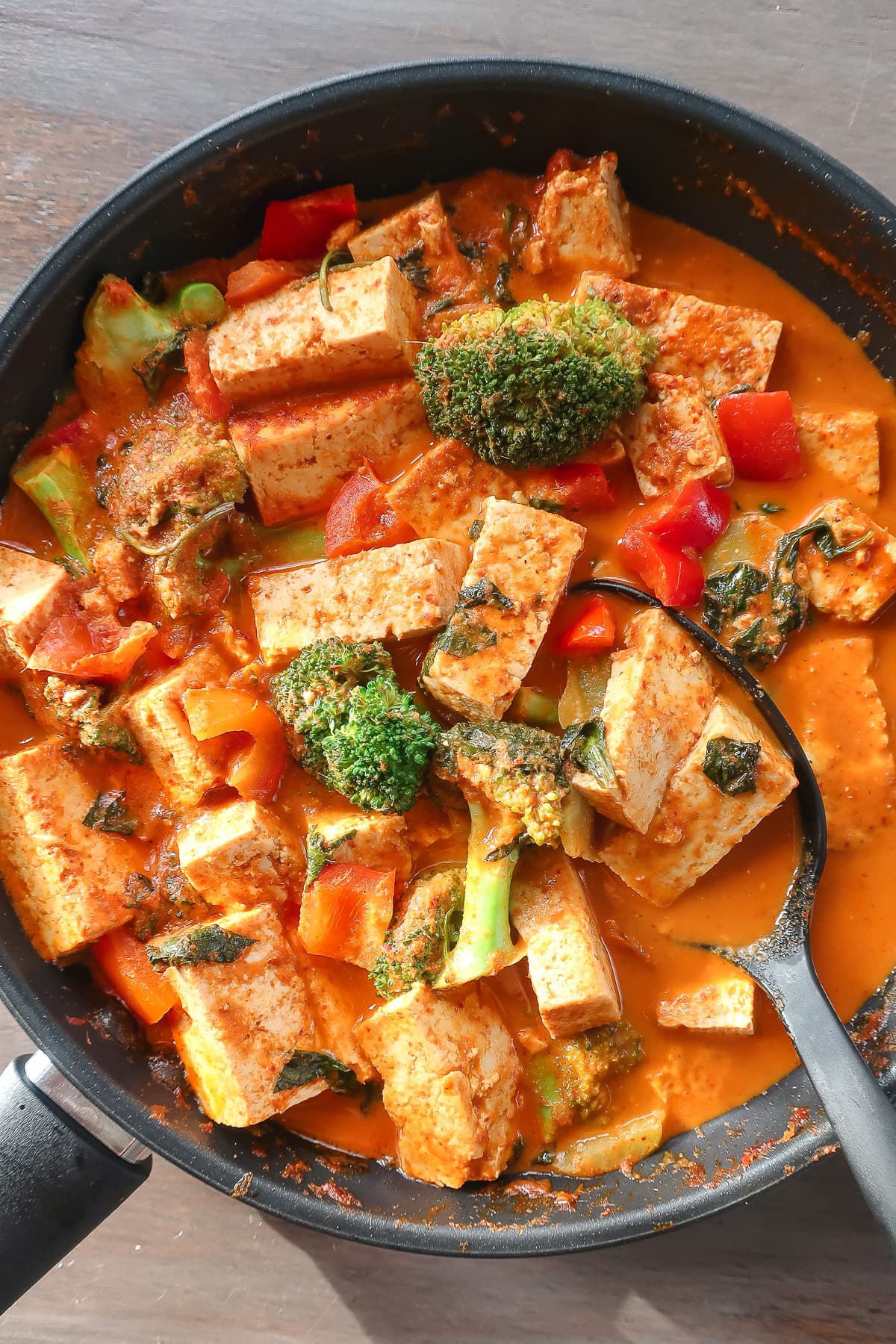thai tofu curry and vegetables in a pan with a large spoon