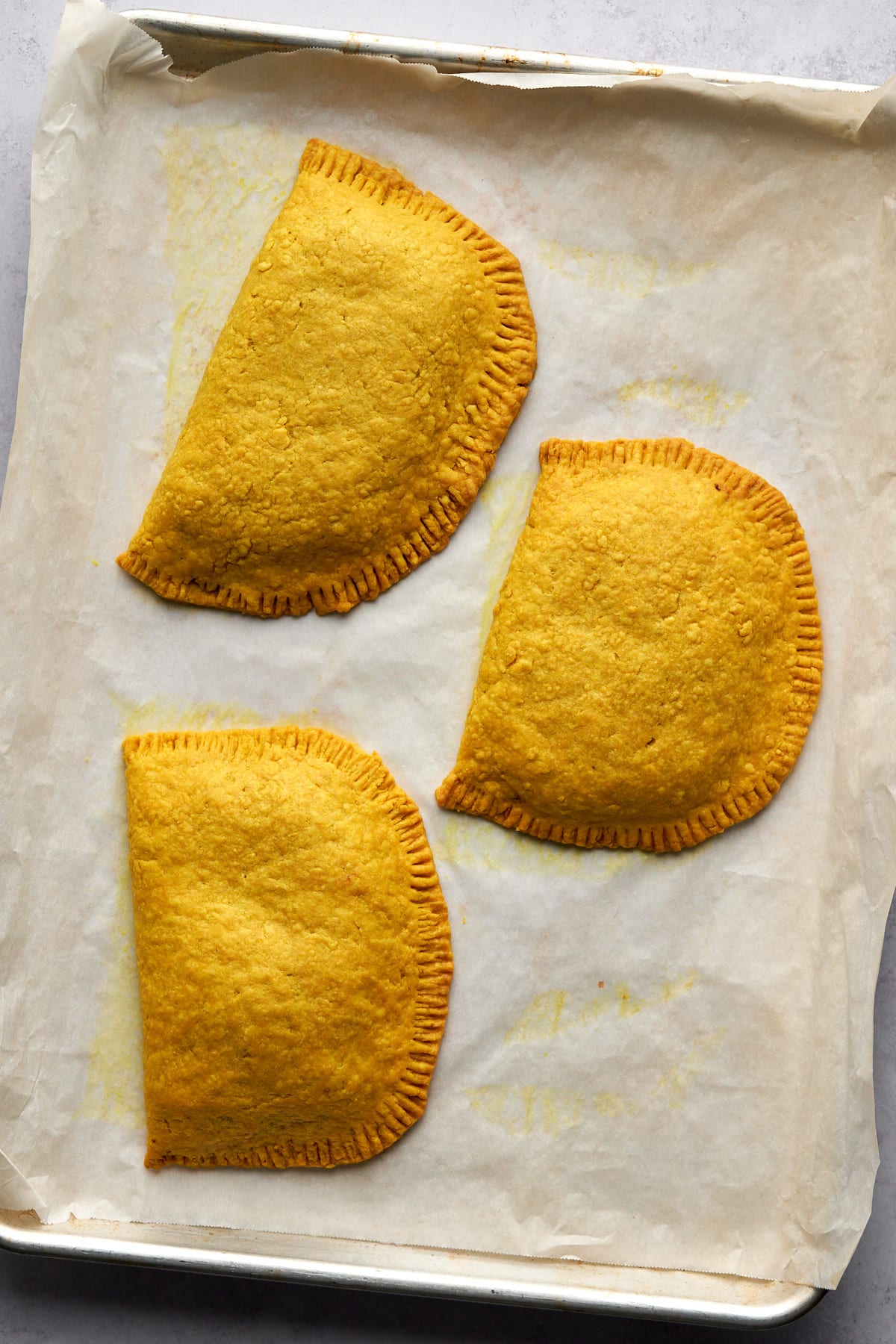 Three baked jamaican patties on baking tray liked with parchment paper.
