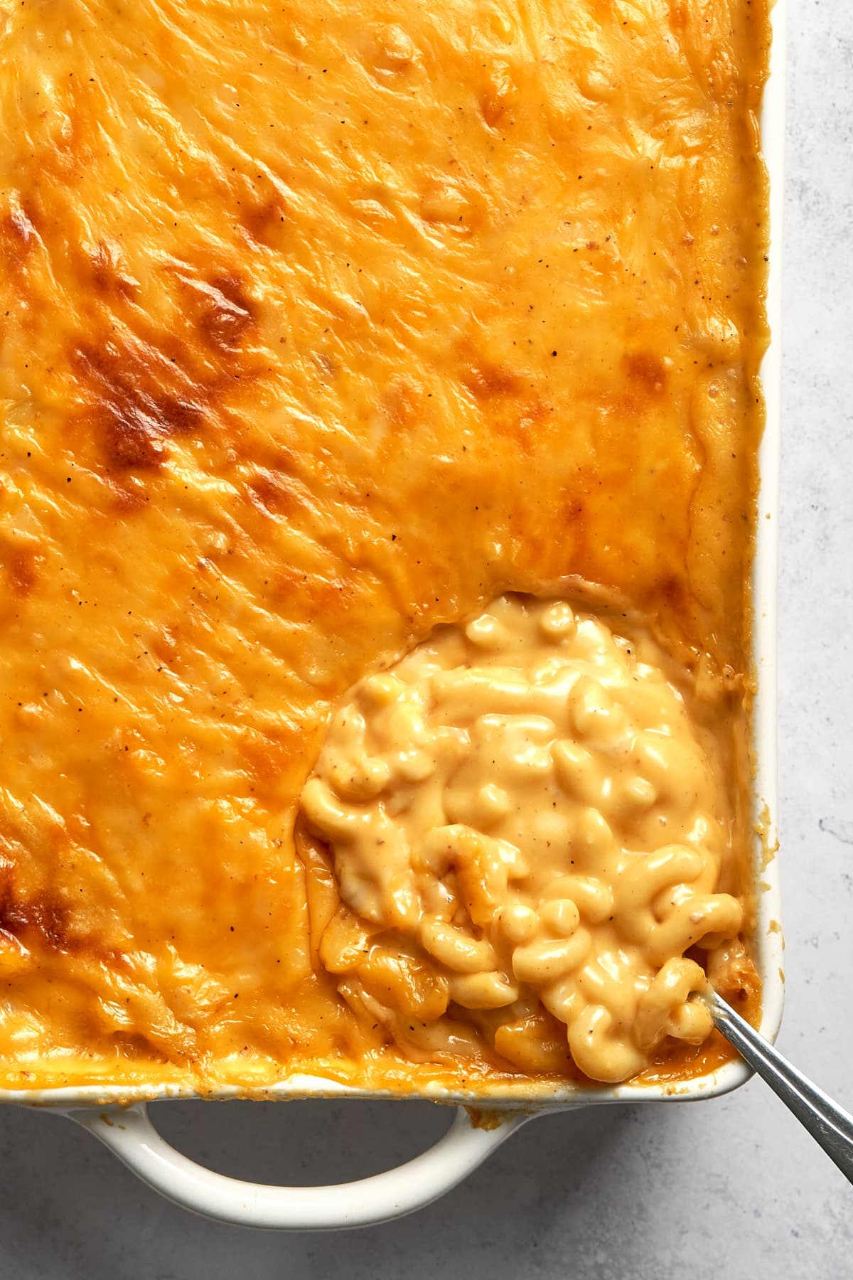 Close up of mac and cheese in a casserole dish being scooped with spoon.